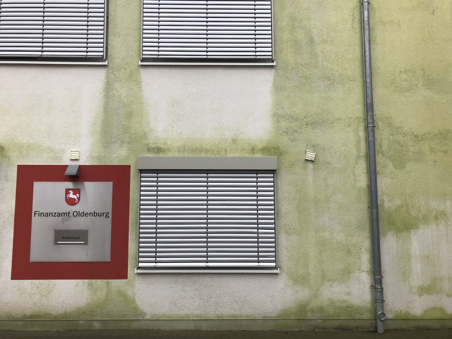 Grün vermooste Wand, darin eingelassen: Briefkasten mit der Aufschrift Finanzamt Oldenburg