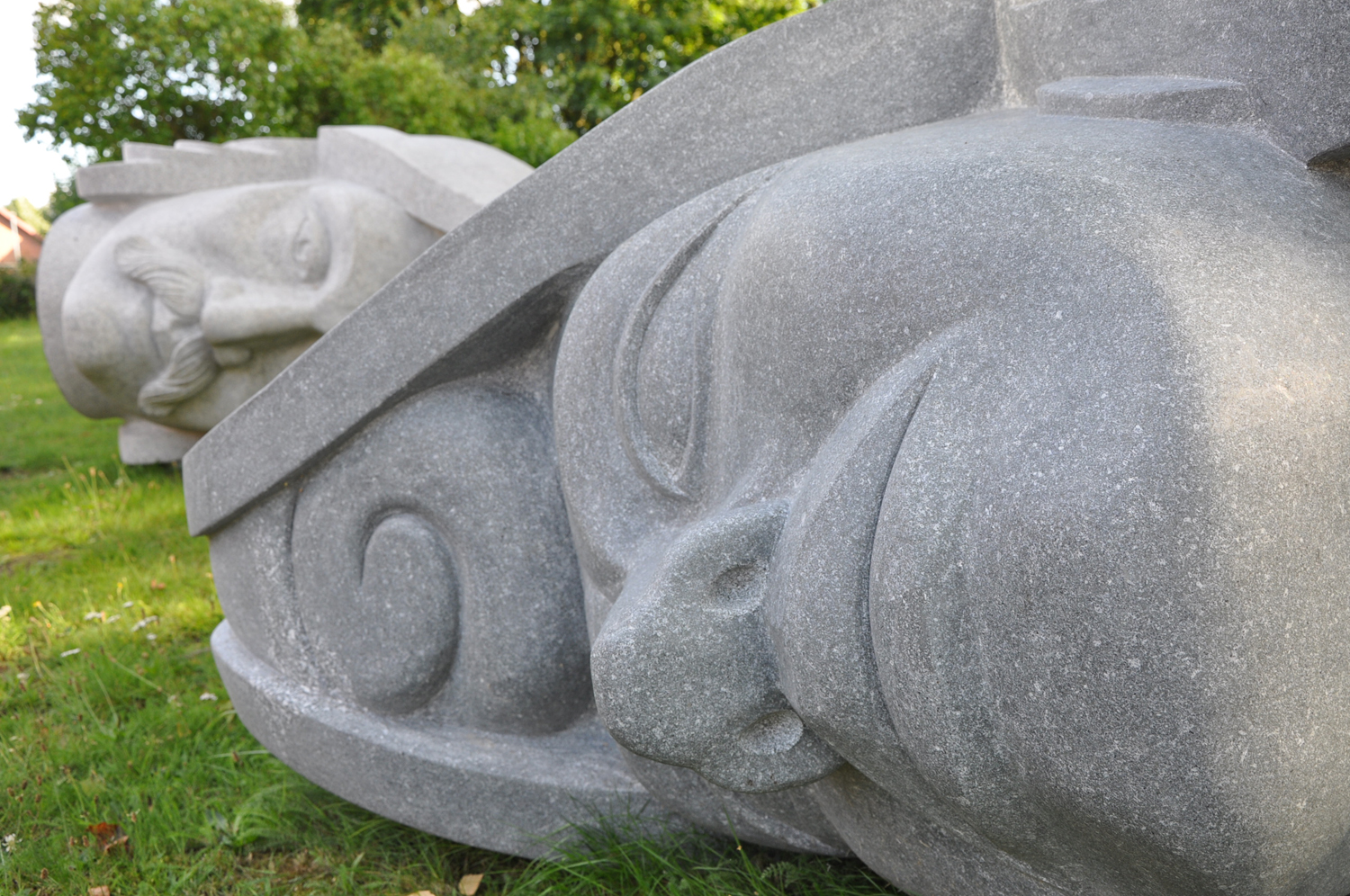 Riesige steinerne Köpfe liegen auf einer Grasfläche vor der Kirche in Bassum.