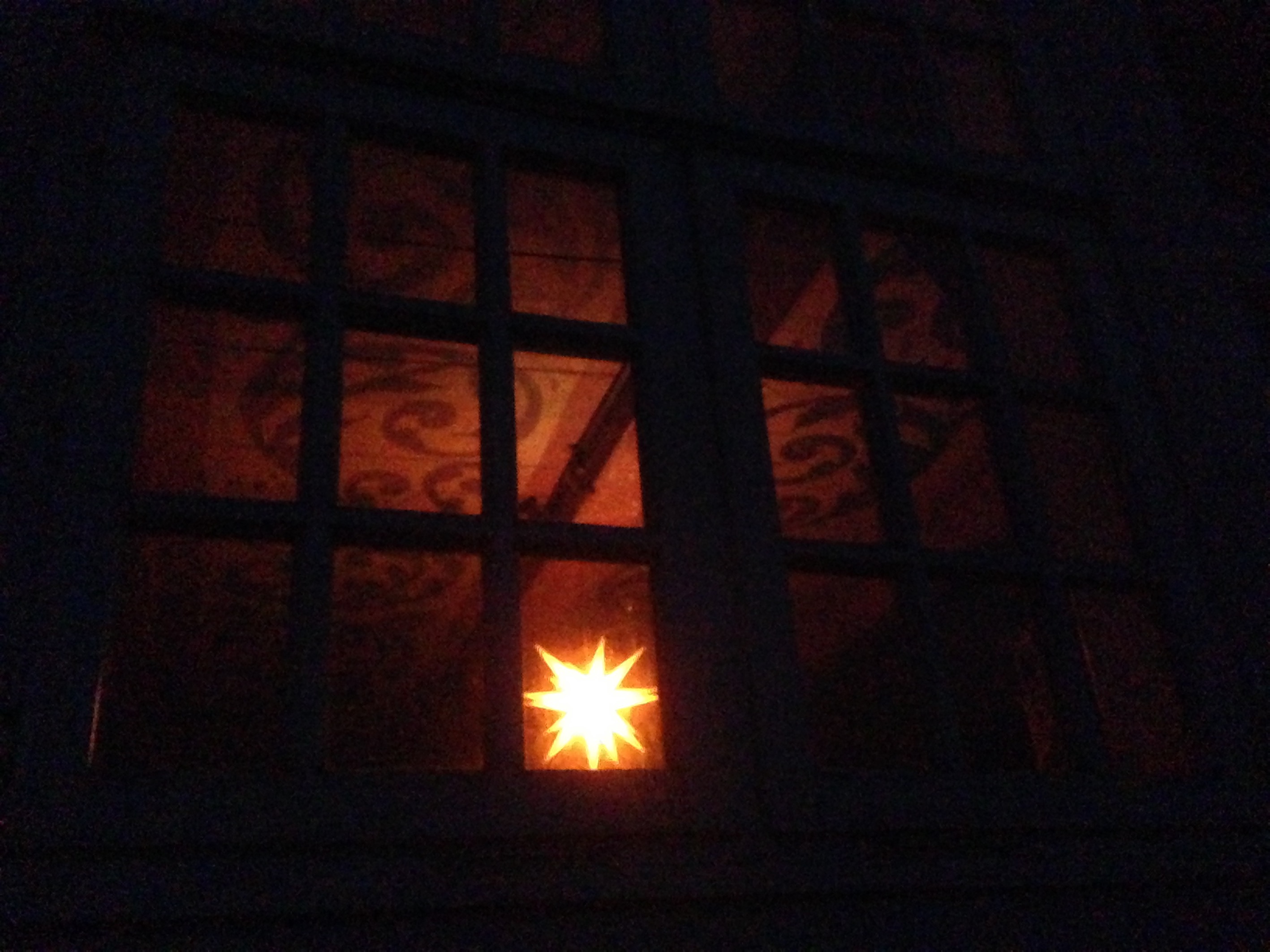 Nächtlicher Blick durch ein Fenster auf einen weihnachtlichen Leuchtstern, der eine bemalte Decke erhellt