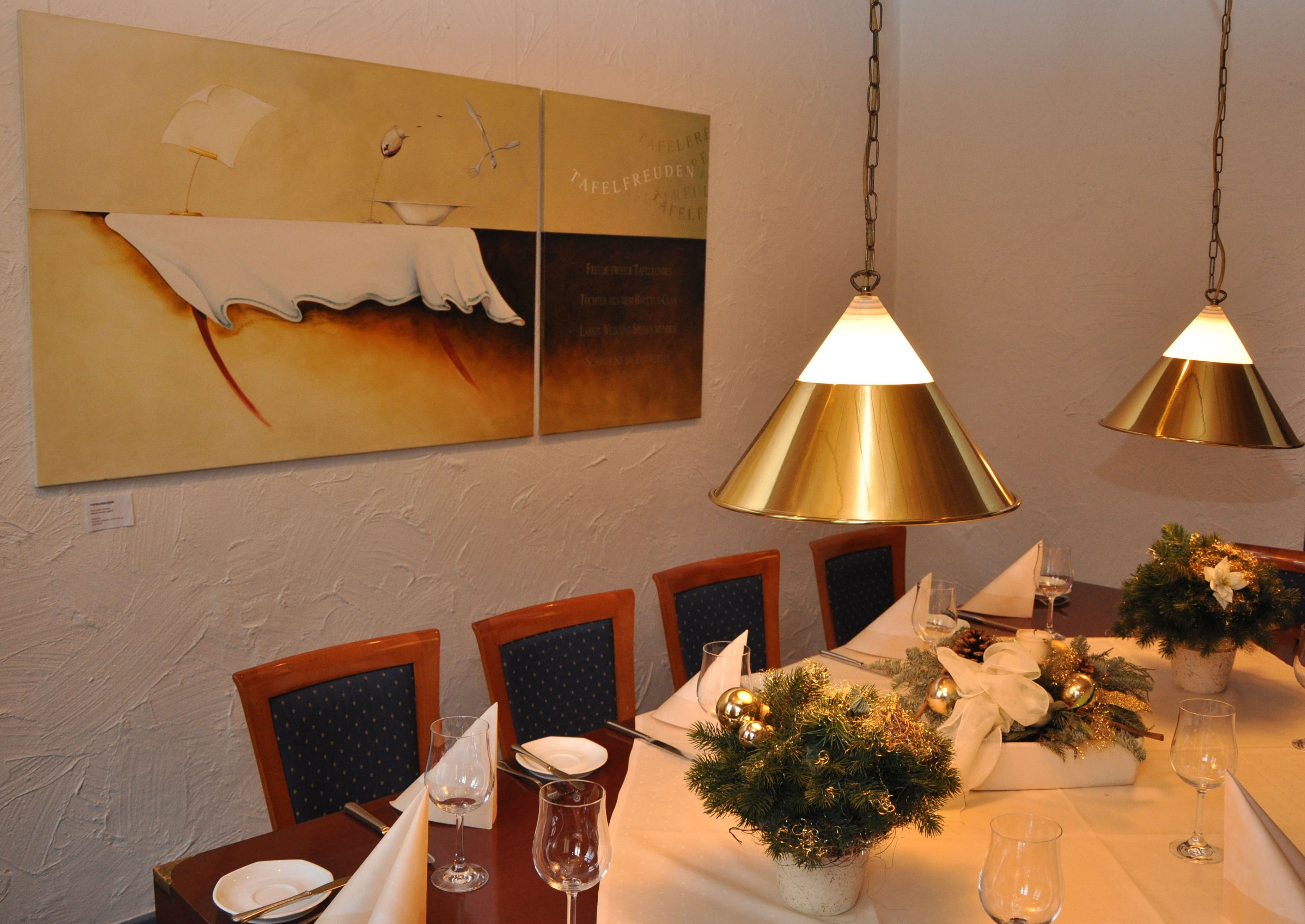 Weihnachtlich gedeckte Tafel in Gaststätte. An der Wand ein Diptychon zum Thema „Tafelfreuden“