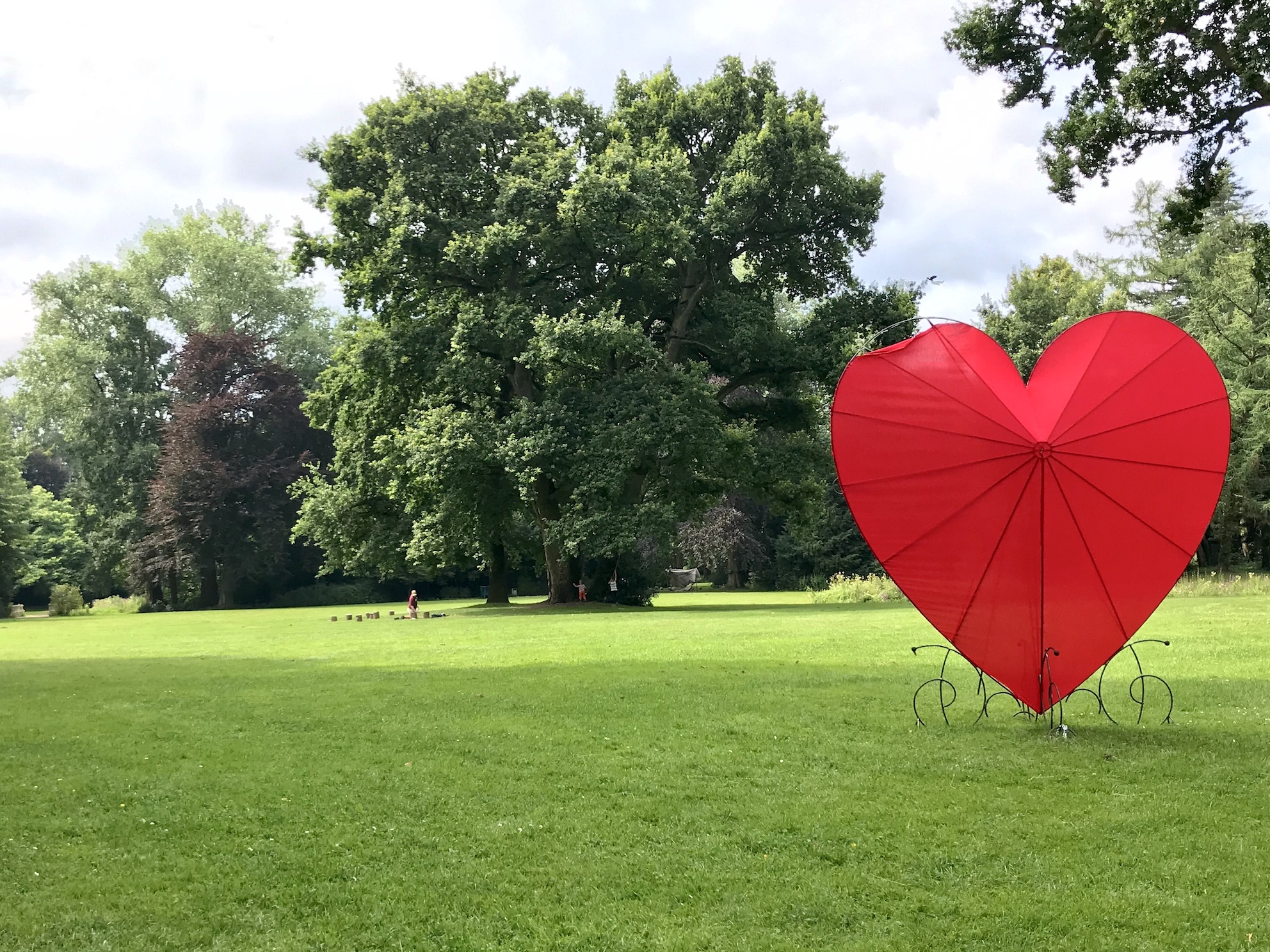 Großes Herz aus Plane auf grünem Rasen im Schlossgarten Oldenburg. Dahinter: großer Baum in Herzform.