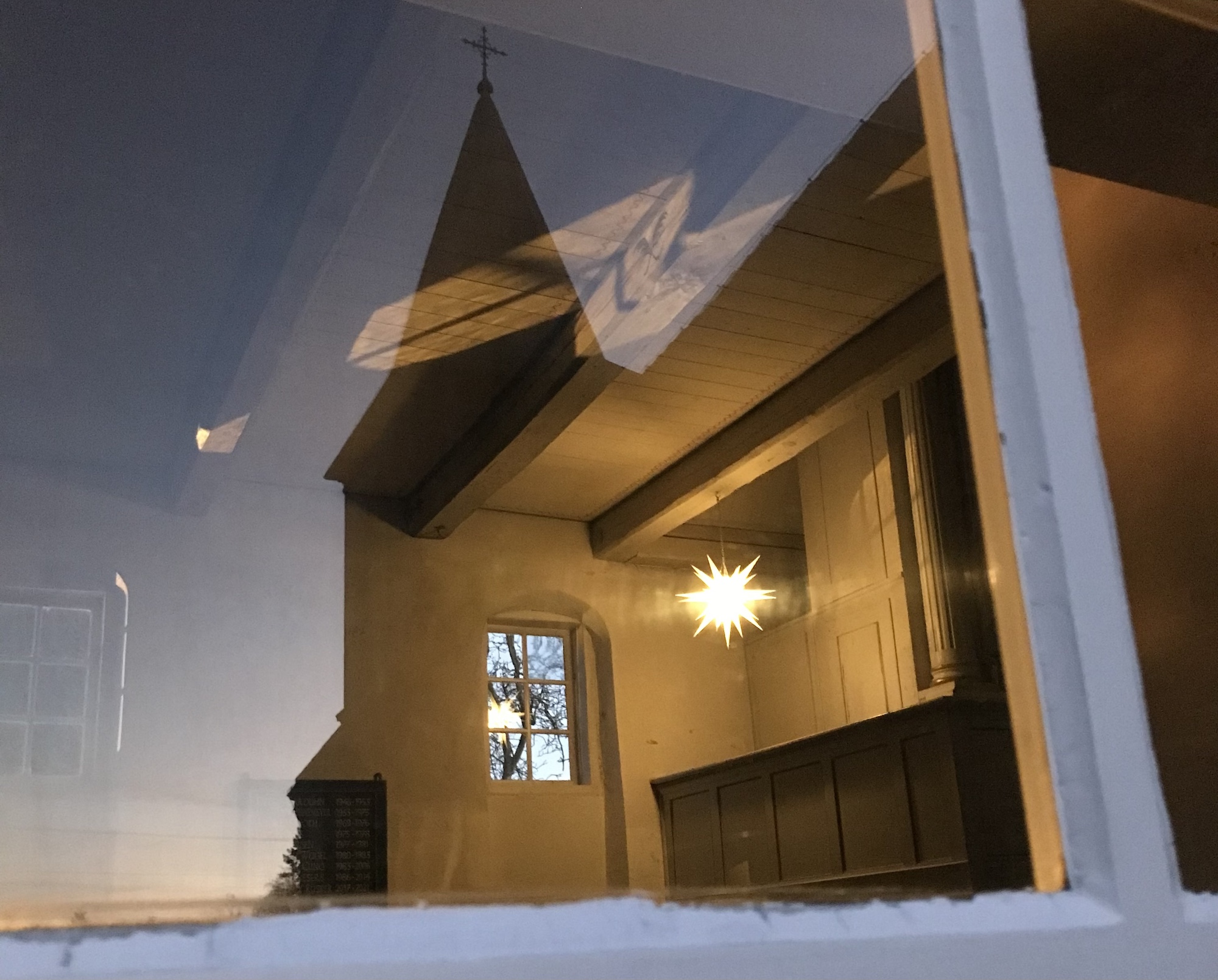 Blick durch ein Fenster ins Innere einer Kirche. Gleichzeitig spiegelt sich der Kirchturm im Fenster.