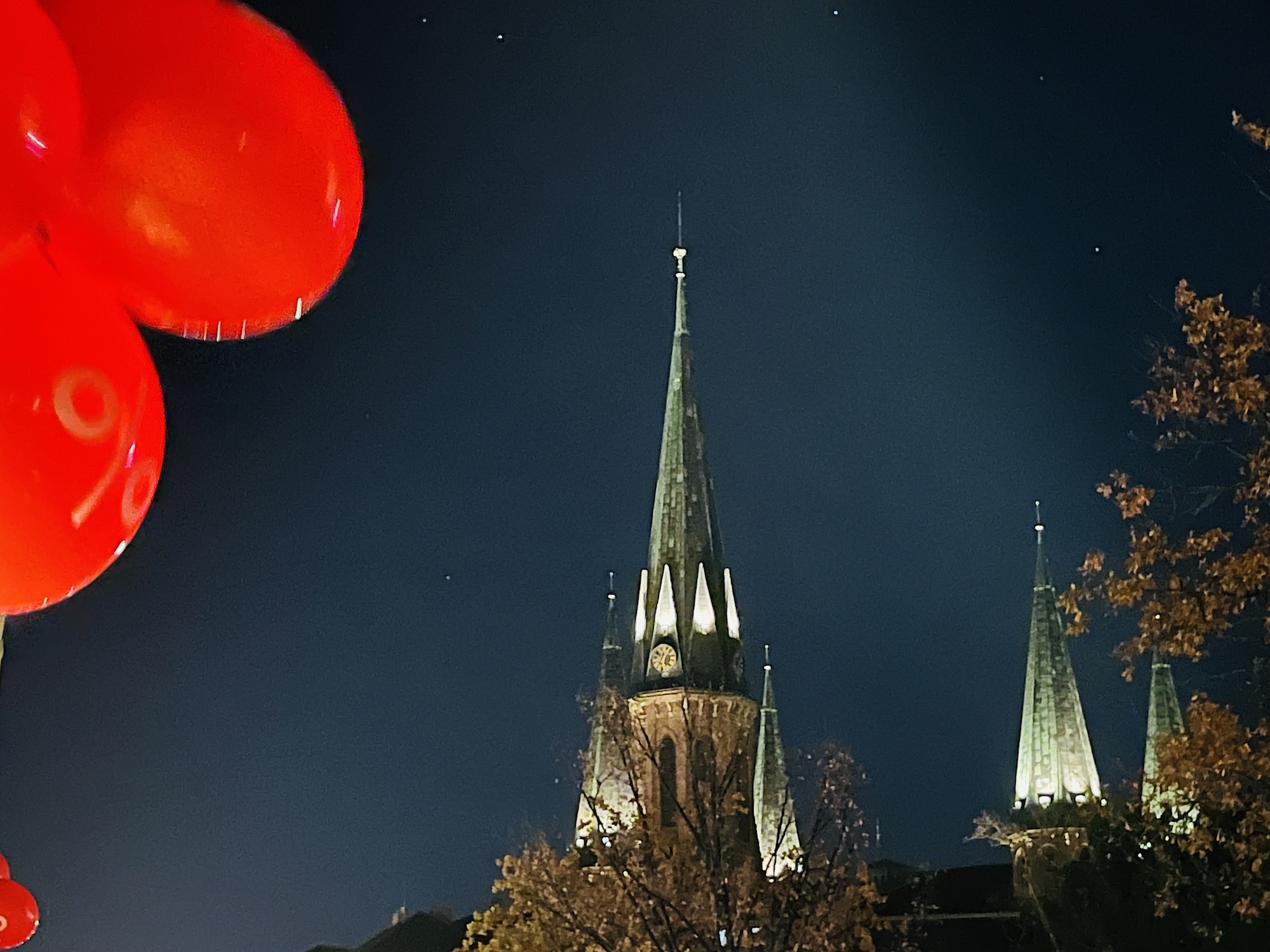 Beleuchteter Kirchturm der Lambertikirche Oldenburg, in der Nacht. Seitlich im Vordergrund: knallrote Luftballons