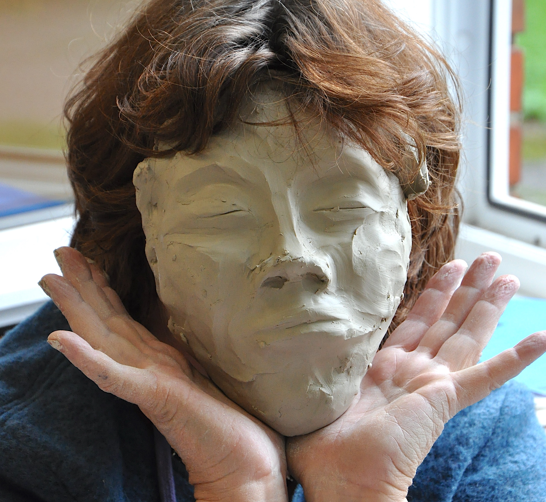 Frau hält sich Maske aus Ton vors Gesicht