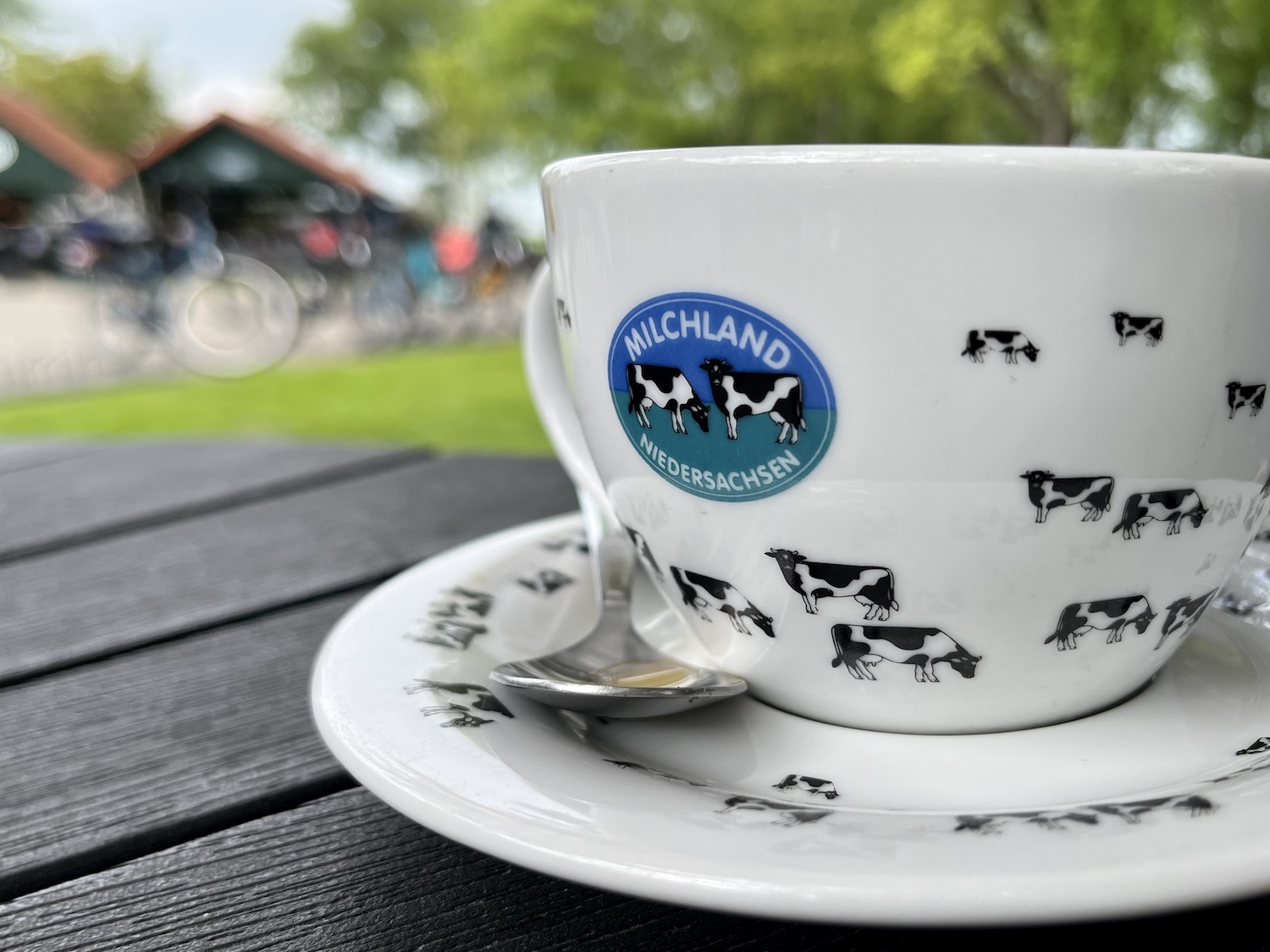 Tasse mit Kuh-Motiven und dem Logo: Milchland Niedersachsen. Im Hintergrund, unscharf: Melkus und Fahrräder