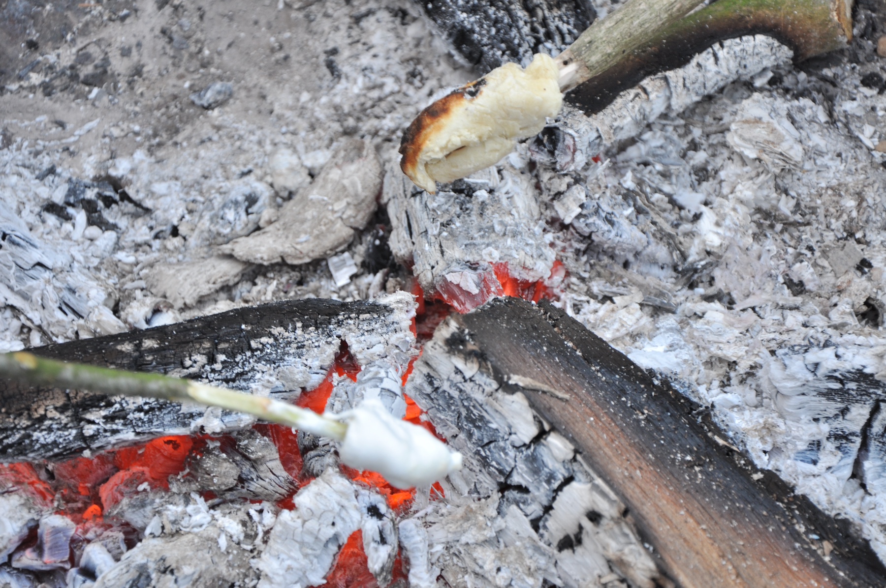 Glut und Asche eines Lagerfeuers. Darin werden Stockbrot und Marshmallows gegrillt.